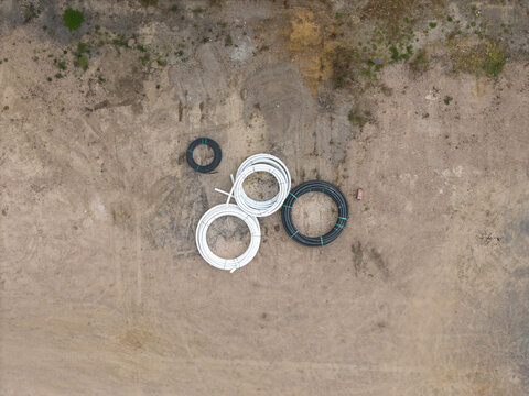 Aerial view of coils of black and white industrial pipes resting on a dirt construction site at Bayswater North Factories in Melbourne, Victoria, Australia.