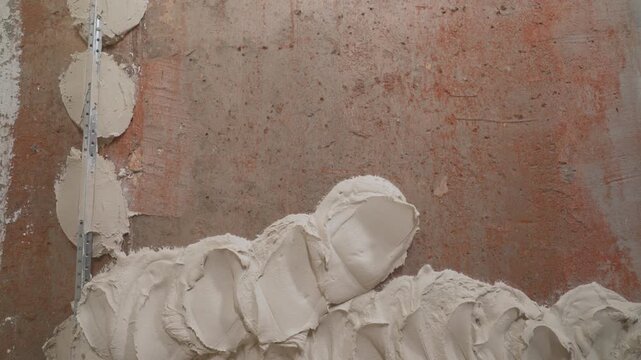 Close up of a construction worker hand in a glove plastering a rough wall. Applying putty or spackle with a trowel during interior finishing work. Home improvement and DIY repair concept