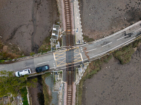 Aerial view of Terras Bridge level crossing with railway tracks intersecting a road marked with yellow box junctions and cars waiting in Looe, Cornwall, United Kingdom.