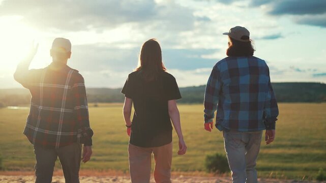 Three farmers walk together across rural field at sunset. Confident farmers move forward through countryside toward open farmland. Team walks side by side under warm evening sky. Rural field.