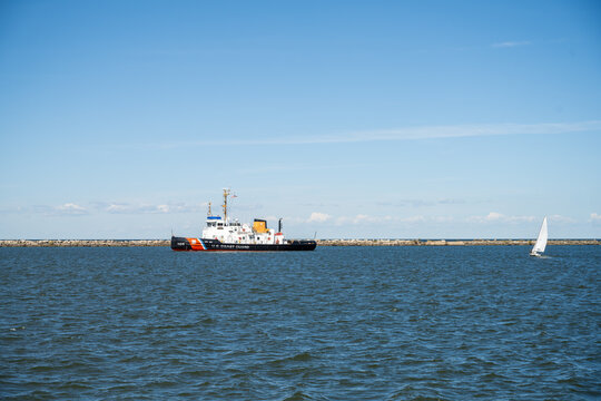 Cleveland, Ohio, United States - 08 October 2026: View of a US Coast Guard cutter patrolling the waters of Lake Erie near a breakwater with a small sailboat nearby under a clear blue sky.