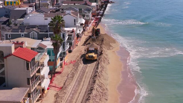 Long Beach, California, USA - October 15, 2026: Loaded dump truck drives up to an excavator spreading sand into a protective berm in front of beachfront homes after Tropical Storm Rachel.