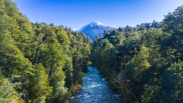 Ruca Malen River flows through dense Patagonian forest beneath a snow capped mountain in Neuquen, Argentina.
