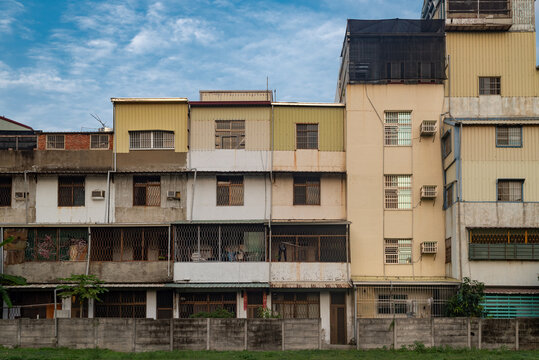 Tainan, Taiwan - 12 May 2015: View of a row of traditional residential buildings with metal security grilles, balconies, and varied facade colors under a blue sky.