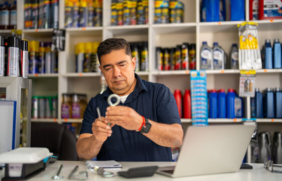 Mature man holding an auto part, working in his hardware store