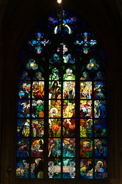 Prague, Czechia - 05 October 2026: View of the intricate stained glass window in St. Vitus Cathedral, featuring vibrant religious scenes, detailed figures, and ornate gothic tracery.