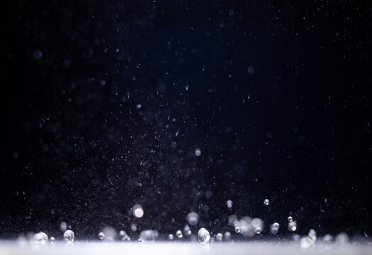 Water droplets falling through a dark space and landing on a lit surface