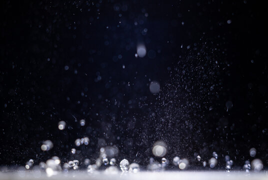 Water droplets falling through a dark space and landing on a lit surface
