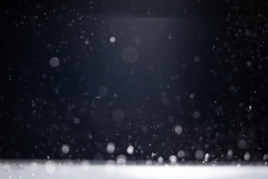 Water droplets falling through a dark space and landing on a lit surface