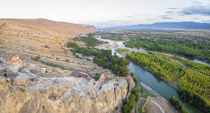 Wide panorama view of Mtkvari river surounded by green nature and Uplistsiche cave town rock formations. Travel in scenic places.Caucasus. Georgia
