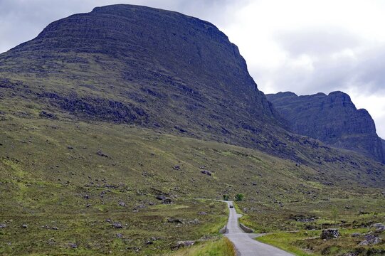 Narrow, single track road, winds through wide, green countryside, high, barren mountains. Applecross, Highlands, Scotland, Great Britain