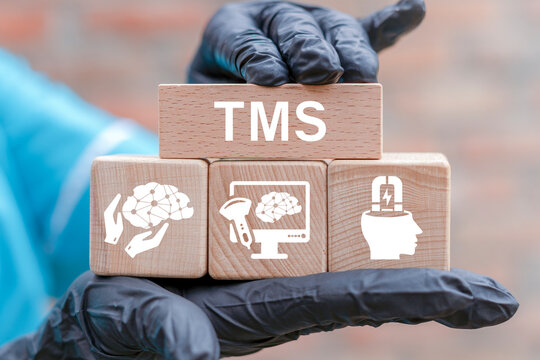 Concept of TMS Transcranial Magnetic Stimulation. Doctor demonstrates TMS abbreviation against background of wooden blocks with icons. Healthcare and modern innovations.