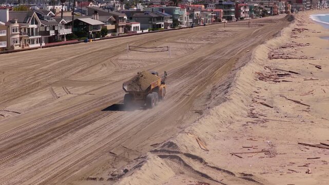 Long Beach, California, USA - October 15, 2026: Articulated dump truck carries sand along a long protective berm as storm debris litters the beach in front of homes after Tropical Storm Rachel.