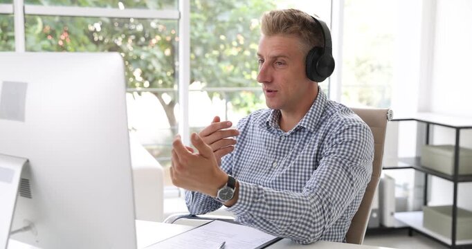 Human resources manager in headphones conducting online job interview via video chat on computer at table indoors