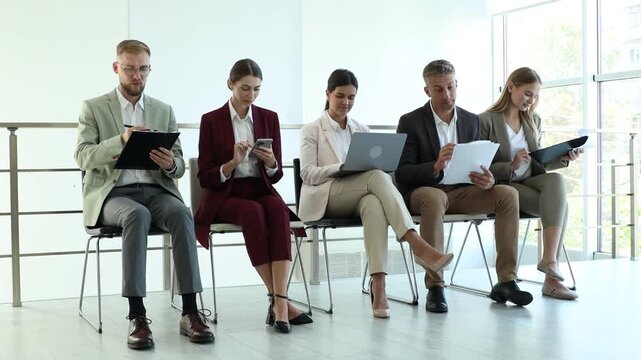Group of people waiting in queue for job interview on chairs indoors