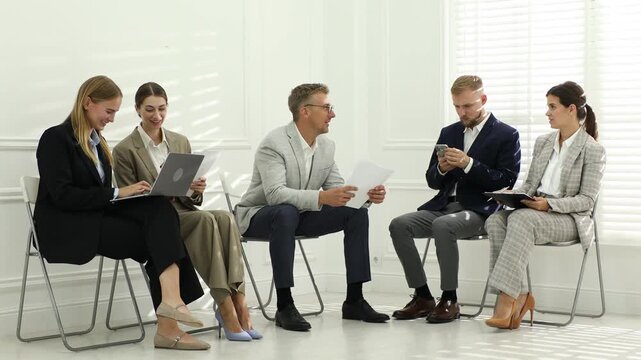 Group of people waiting in queue for job interview on chairs indoors
