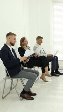 Group of people waiting in queue for job interview on chairs indoors