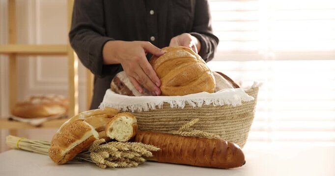 Woman putting bread loaves into basket at light table indoors, closeup