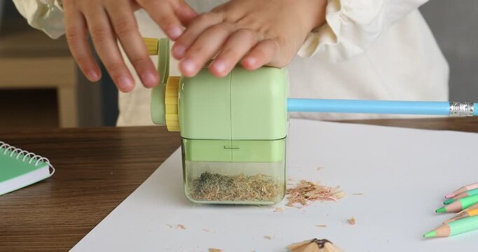 Child using hand-cranked sharpener at table, closeup