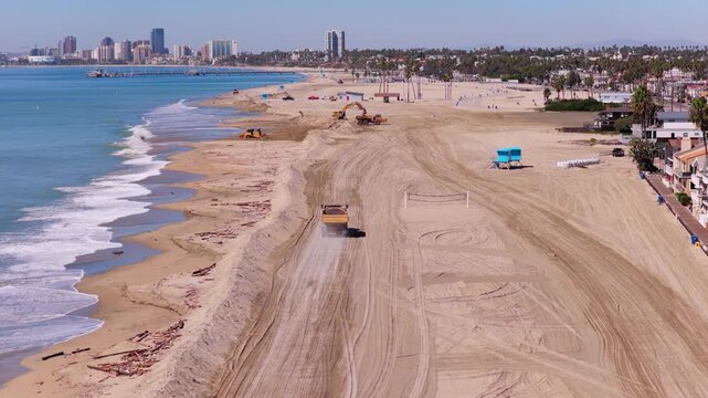 Long Beach, California, USA - October 15, 2026: Dump truck, excavator and bulldozer build a sand berm on a debris strewn beach, Belmont Pier and downtown skyline behind, after Tropical Storm Rachel.