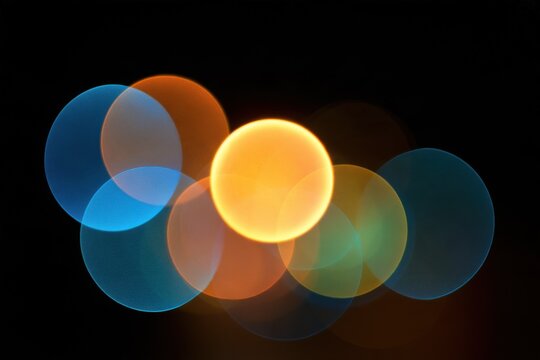 Colorful round bokeh lights in blue, orange, yellow and green on black background, defocused glowing circles for festive holiday design art