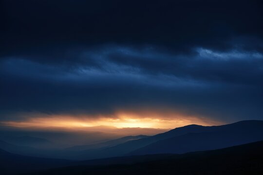 Layered mountain silhouettes under dark blue sky with golden light breaking through clouds, calm evening atmosphere for nature landscape design art