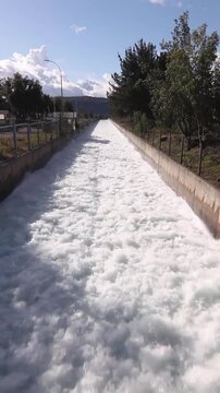 Vertical stock footage of straight concrete hydroelectric discharge channel with turbulent foaming water