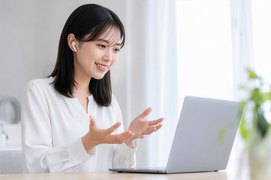 若い女性が笑顔でジェスチャーを交えながらノートパソコン越しに会話する｜オンライン会議・リモートワーク・ビデオ通話・在宅勤務のイメージ