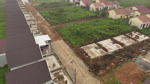 A view from above of a row of rooftops next to a green field and a concrete road in a new housing development.