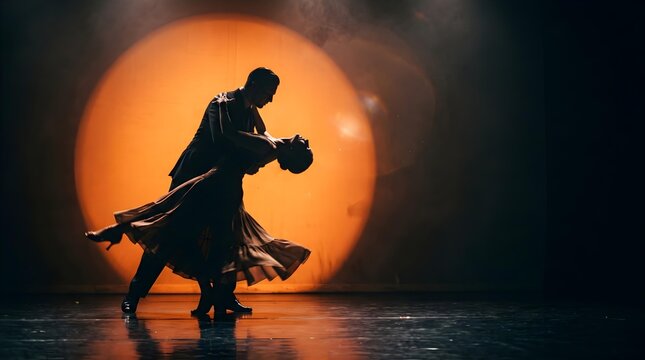 Silhouette of elegant couple dancing tango in dramatic orange spotlight on stage. Professional dancers performing passionate ballroom dance with flowing dress in theatre. 