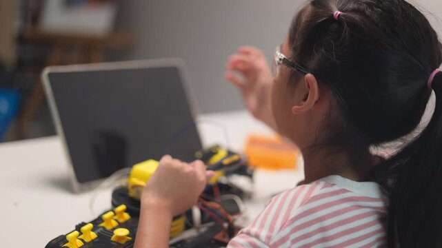 Smart Asian girl in safety glasses building and programming robotic toy car at home desk. Children STEM education, creative technology learning and robotics engineering workshop concept.