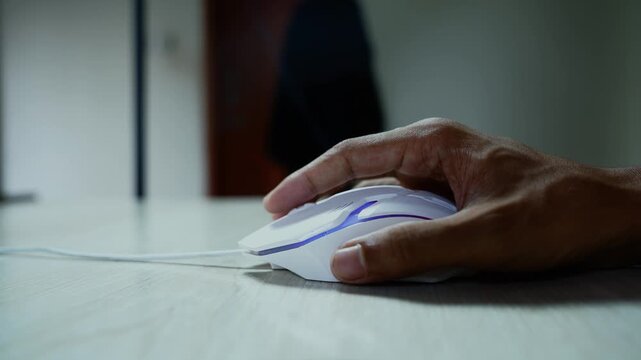 Close-up hand using a computer mouse, Close-up of an adult hand using a white computer mouse on a desk, with a softly blurred indoor background and moody natural light.