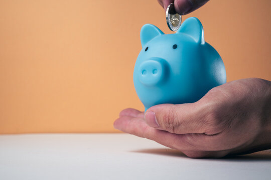 Saving money concept hand inserting a banknote into a blue piggy bank with coins. Representing the budget, personal finance, and wealth-building concept