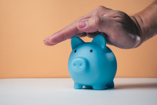 Saving money concept hand inserting a banknote into a blue piggy bank with coins. Representing the budget, personal finance, and wealth-building concept