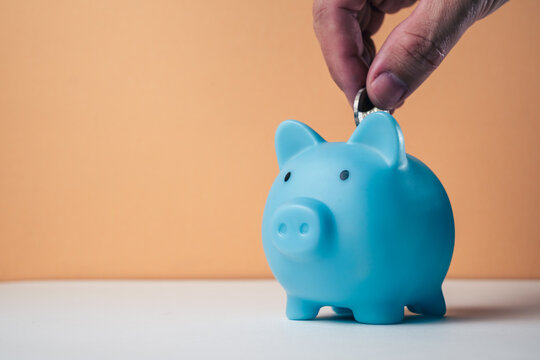 Saving money concept hand inserting a banknote into a blue piggy bank with coins. Representing the budget, personal finance, and wealth-building concept