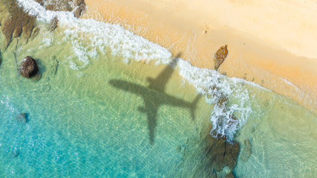 Aerial view of shadow passenger plane silhouette and sandy beach blue sea with waves at sea beach summer vacation sea travel concept	