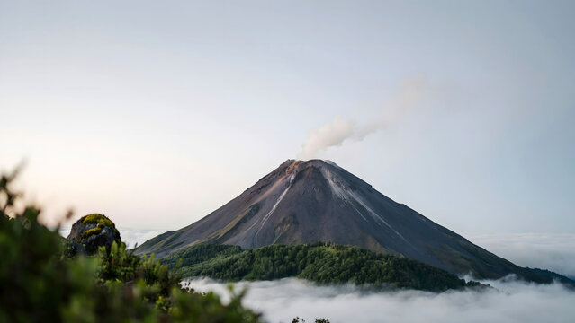 Arenal volcano in costa rica with smoke emitting from the summit above a forest and sea of clouds