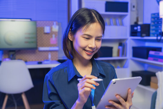 Young Asian businesswoman using tablet with stylus while working in modern office, digital productivity and technology concept.