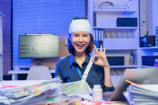 Injured young Asian businesswoman shows ok sign while recovering at office.