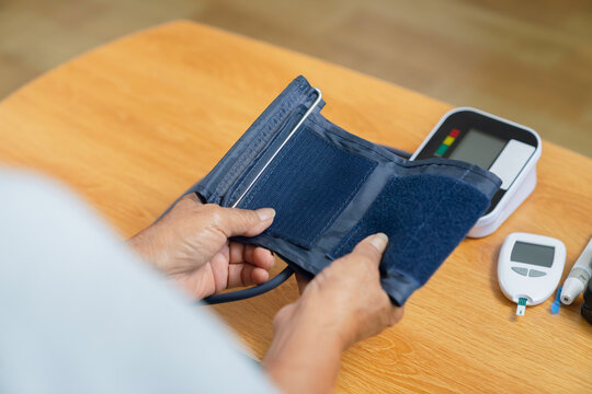 Elderly woman holding measuring her blood pressure with a digital monitor, personal wellness, health monitoring.