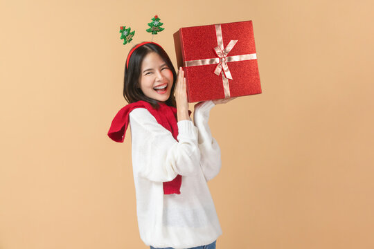 Cheerful Asian woman wearing a white sweater and holding red gift box while smiling.