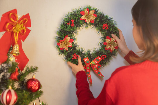 Christmas wreath hanging on a wall, with a hand adjusting the festive decoration, holiday preparation.
