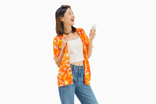 Happy smiling young Asian woman in summer wearing floral shirt holding fan to cool herself with suffers from too hot weather in white background