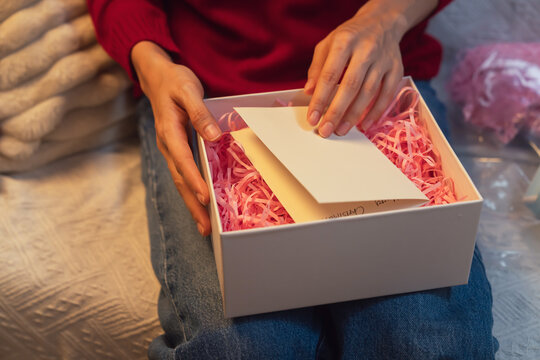 woman in a red sweater opening a gift box with a greeting card inside, Christmas present and holiday gift giving.