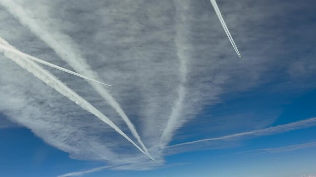 immersive pilot perspective doing a right turn in a busy air traffic route in the upper atmosphere, with multiple jet contrails in a blue sky, flying under a layer of cirrus clouds