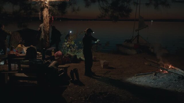 Group of people camping on the river's coast at night. People camping on a river as seen from the forest