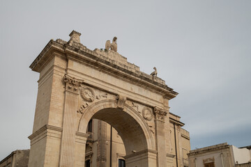 Limestone Porta Reale triumphal arch illuminated under a cloudy sky in Noto, Sicily. © Uvamenfoto