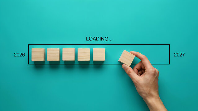 Hand placing wooden block inside progress bar loading towards year twenty twenty seven on turquoise background