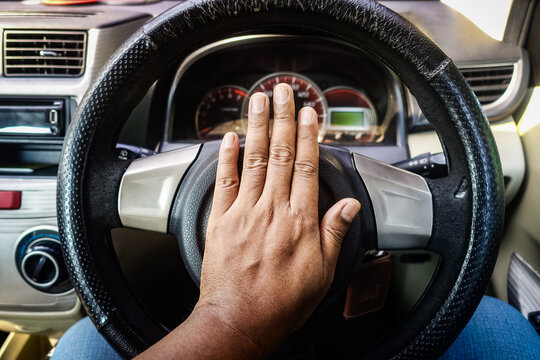 driver's hand pressing on the center of a black car steering wheel, honking the horn 
