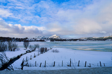Beautiful winter landscape of a frozen lake and snow-covered plains in Lofoten Islands, Norway. Majestic mountain peak under blue sky with dramatic clouds. Scenic Arctic nature view of Scandinavian ro © bank215